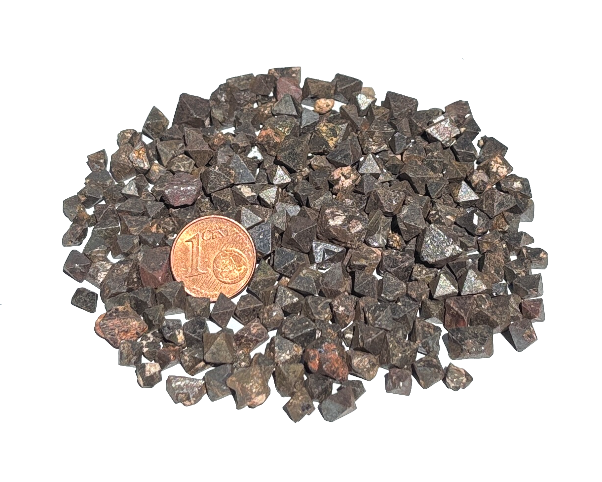 Vielzahl an Magnetit Oktaedern auf weißem Hintergrund im Größenvergleich mit einem Pfennig
