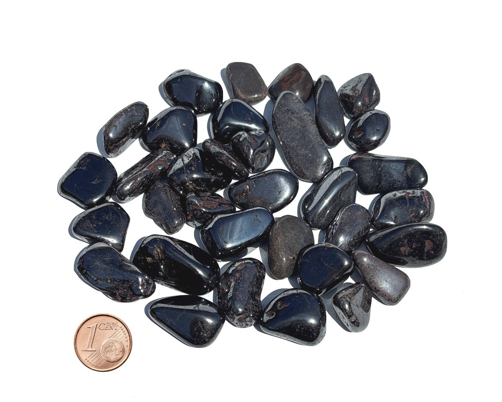 Vielzahl an Magnetit Trommelsteine mit Pfennig Größenvergleich auf weißem Hintergrund