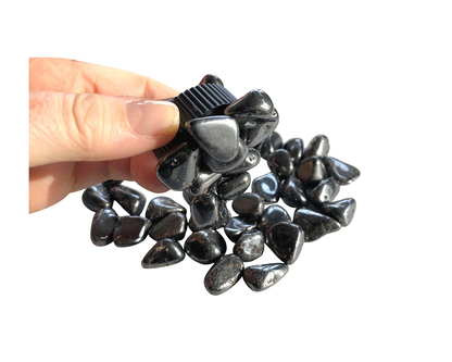 Magnetit Trommelsteine mit Magnet in der Hand auf weißem Hintergrund